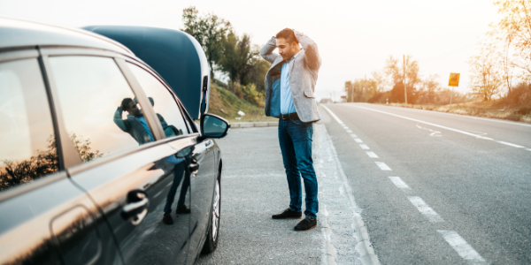 Man looking stressed while stranded with broken down car on the side of the road.