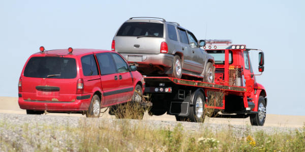 Two cars being hauled by one red wrecker.